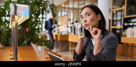 Doubtful Asian business woman talking on phone making call and thinking. Stock Photo
