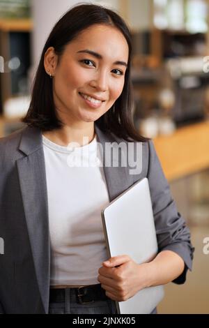 Smiling young Asian professional woman wearing suit, vertical portrait. Stock Photo