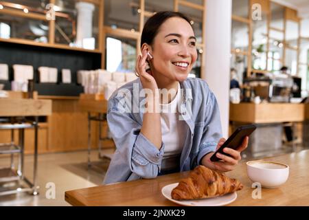 Young smiling Asian woman student using smartphone listening podcast. Stock Photo
