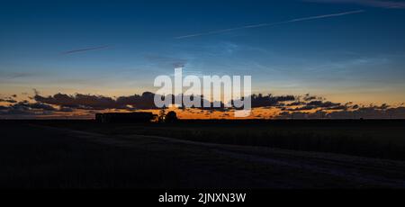 Panoramic view of ragged dark clouds, shiny noctilucent clouds and colorful twilight sky above an agricultural landscape Stock Photo