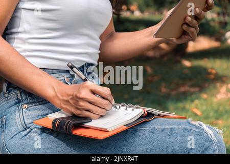 Smiling asian woman writing in a notebook and laptop. Summer in the park Stock Photo