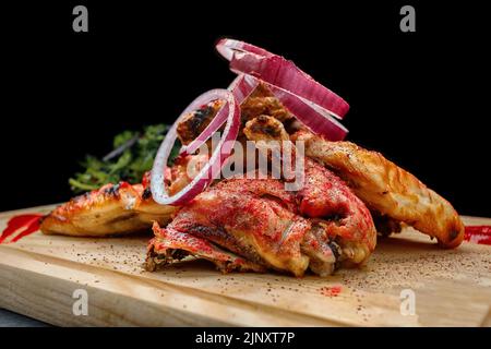 Chicken with tkemali sauce and onions on a wooden board on a black background Stock Photo