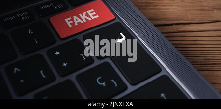 Banner close up of laptop keyboard with "fake" text on button and selective focus. Red button with fake text on it. Fake news concept. Stock Photo