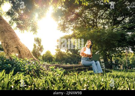 Smiling asian woman writing in a notebook and laptop. Summer in the park Stock Photo