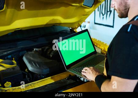 Hands of young repairman or technician typing on laptop keypad while standing in front of open hood of car and making diagnostics Stock Photo