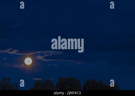 Beautiful nature landscape view of bright moon in night cloudy sky over trees tops. Sweden. Stock Photo