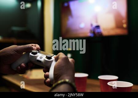 Hands of young African American man pressing buttons on controller while directing device on screen of tv set during video game Stock Photo