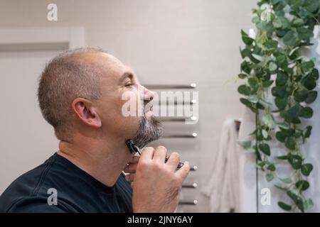 Middle-aged handsome man using razor in bathroom Stock Photo