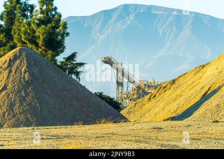 Stone quarry crusher and belt conveyor as seen between piles of stone aggregate. Stock Photo