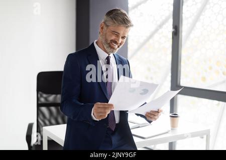 Successful Entrepreneurship Concept. Happy Mature Businessman In Suit Checking Financial Papers Stock Photo