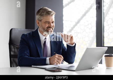 Handsome smiling middle aged businessman using laptop and writing in notepad Stock Photo