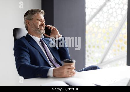 Happy Mature Businessman Having Work Break, Talking On Cellphone And Drinking Coffee Stock Photo