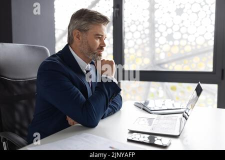 Pensive Middle Aged Businessman Working With Laptop At Desk In Office Stock Photo