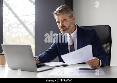 Busy Mature Businessman Working With Laptop And Documents In Office Stock Photo