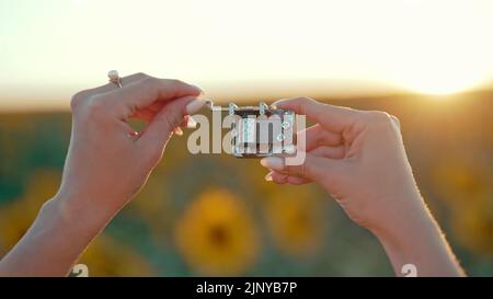 Female hands rotating gears of old music box mechanism. Lady turning the lever of retro small metallic carillon. Woman in sunflowers field listening Stock Photo