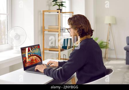 Caucasian man playing in online casino using laptop looking at monitor with roulette wheel Stock Photo