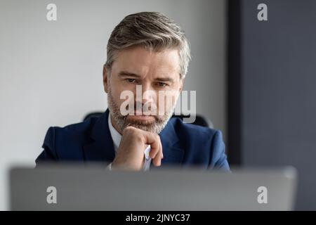 Portrait Of Focused Middle Aged Businessman Looking At Laptop Screen In Office Stock Photo