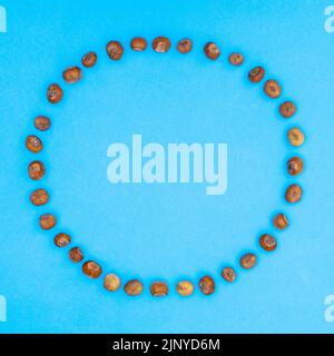 Hazelnuts circle copy space frame on vibrant blue background. Creative flat lay autumn concept Stock Photo