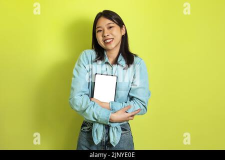 Cheerful Asian Woman Hugging Tablet With Empty Screen, Yellow Background Stock Photo