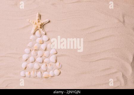 Creative Christmas tree made of shells background of sea sand. Concept tropical new year by the sea Stock Photo