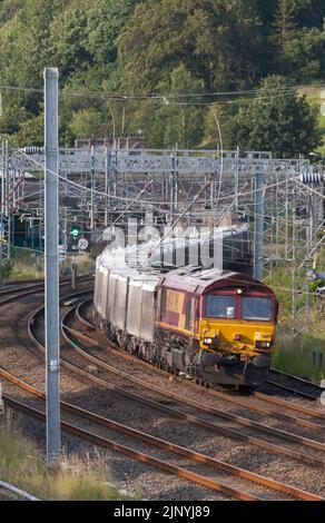 DB Cargo Rail UK class 66 diesel locomotive hauling a freight train on the electrified west coast mainline passing Oxenholme loops, Cumbria Stock Photo