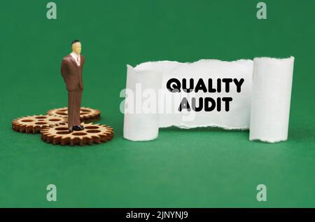 Business concept. The figure of a man stands on the gears and reads the inscription - Quality Audit on paper Stock Photo