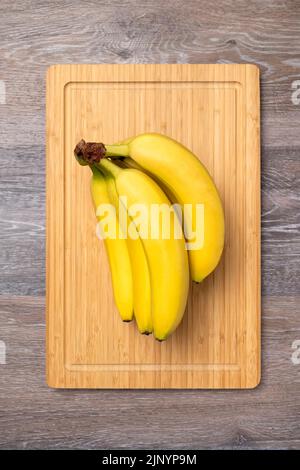 Branch of ripe bananas on a kitchen board, top view Stock Photo