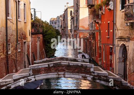 The architectural detail of an old bridge made with red bricks on the typical canal in Venice Stock Photo