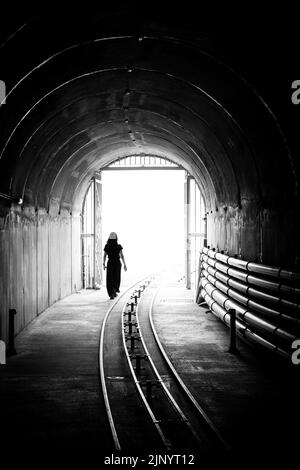 Silhouette of a young woman walking out of a dark tunnel into a bright light. Stock Photo