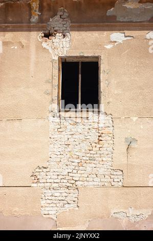 Exterior of old crumbling building has a single window that you can see with a wood frame that may have glass. This is a closeup view. Stock Photo