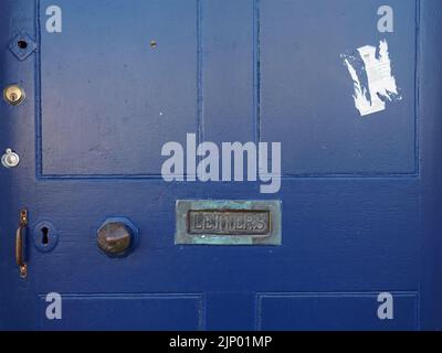 antique letterbox with oxidised verdigris and lettering LETTERS set in old blue painted panelled wooden door alongside brass door-handle Stock Photo