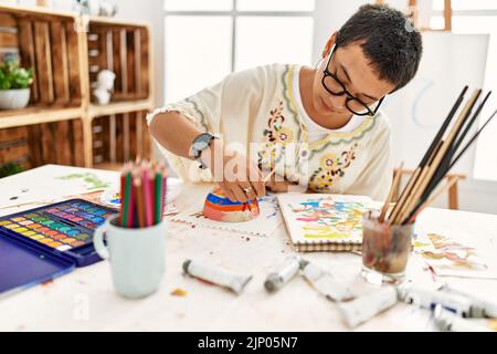 Young hispanic woman painting clay ceramic at art studio Stock Photo
