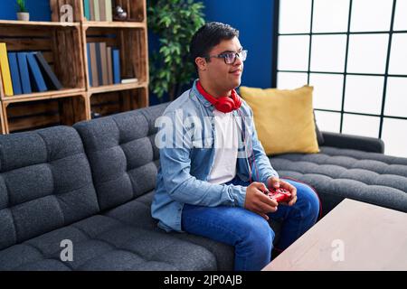 Down syndrome man playing video game sitting on sofa at home Stock Photo