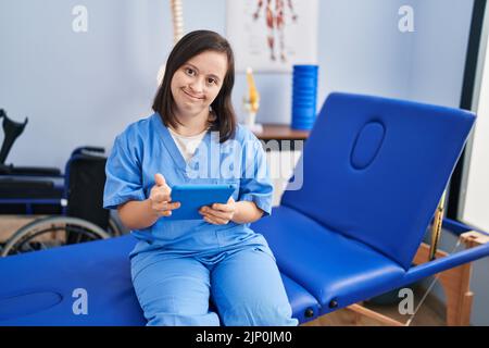 Down syndrome woman wearing physiotherapy uniform using touchpad at physiotherapist clinic Stock Photo