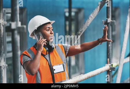 Construction worker talking on a phone call while standing in an empty building. Professional builder discussing plans and strategy, checking the Stock Photo