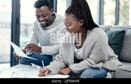 Happy African American couple doing finance planning, writing budget paperwork on sofa at home. Smiling boyfriend and girlfriend discussing insurance Stock Photo