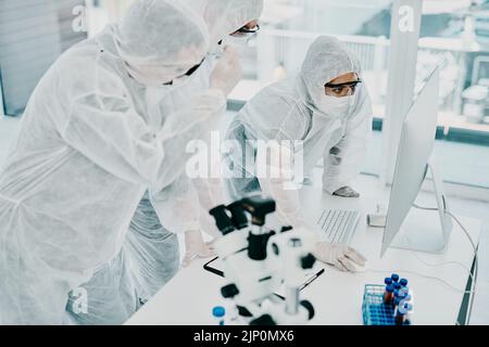 Group of doctors and scientists using computer for medical research on viruses dressed in hazmat suits, for coronavirus cure. Innovation researchers Stock Photo
