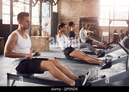 For a full body workout try the rowing machine. a young woman working out with a rowing machine in the gym. Stock Photo