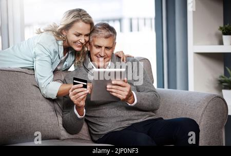 Indulging in a shopping spree of their own. a mature couple using a digital tablet and credit card to do online shopping at home. Stock Photo