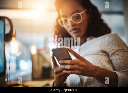 Staying late tonight, dont wait up. a young businesswoman using a mobile phone during a late night at work. Stock Photo