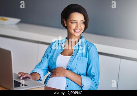 Thank goodness the days of stressful commuting is behind me. a pregnant young woman using a laptop while working from home. Stock Photo