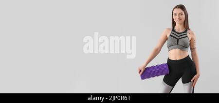 Sporty woman holding foam roller on grey background with space for text Stock Photo