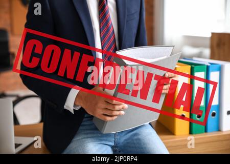 Young man holding folder with top secret documents in office Stock Photo