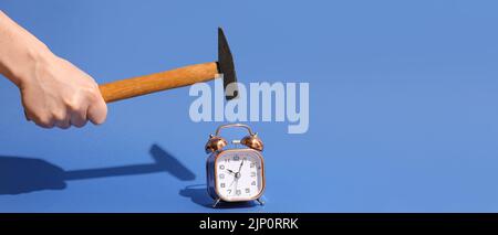 Hand with hammer and alarm clock on blue background Stock Photo