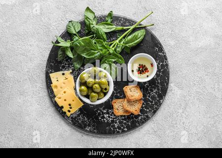 Board with bowl of tasty green olives, oil, cheese, crackers and basil on light background Stock Photo