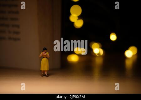 Miniature people toy figure photography. A girl reading a book at night with bokeh defocused light lamp, bed time routine before sleep. Image photo Stock Photo