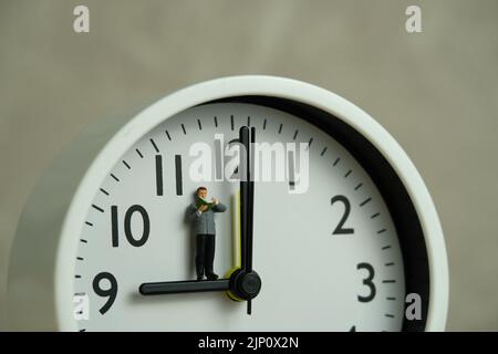 Miniature people toy figure photography. Reading routine concept. A men student standing read a book above clock. Image photo Stock Photo