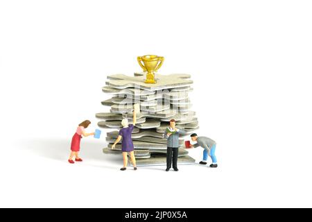 Miniature people toy figure photography. A group of student standing above puzzle jigsaw stack, with golden trophy above it, isolated on white backgro Stock Photo