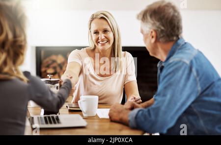 Financial advisor shaking hands with a female client after helping with budget, making a deal and planning with documents at home. Husband and wife Stock Photo