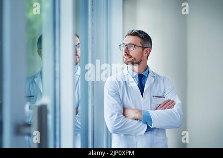 Its been a long but successful shift. a mature doctor looking out the window in a hospital. Stock Photo